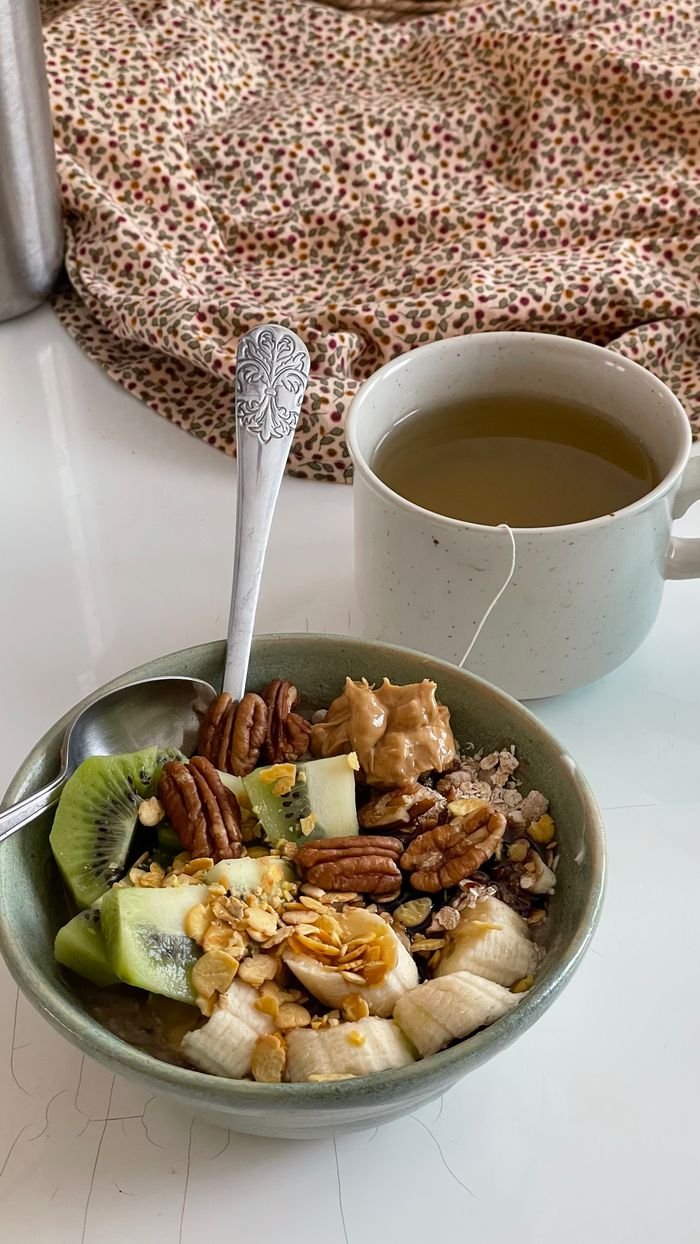 A nutritious breakfast with granola, kiwi, nuts, and a cup of green tea, set on a cozy cloth background.