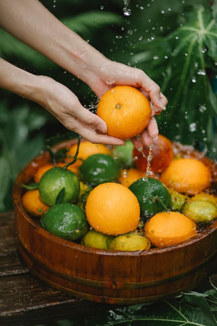 From above crop anonymous female washing fresh juicy tangerines in bowl in garden